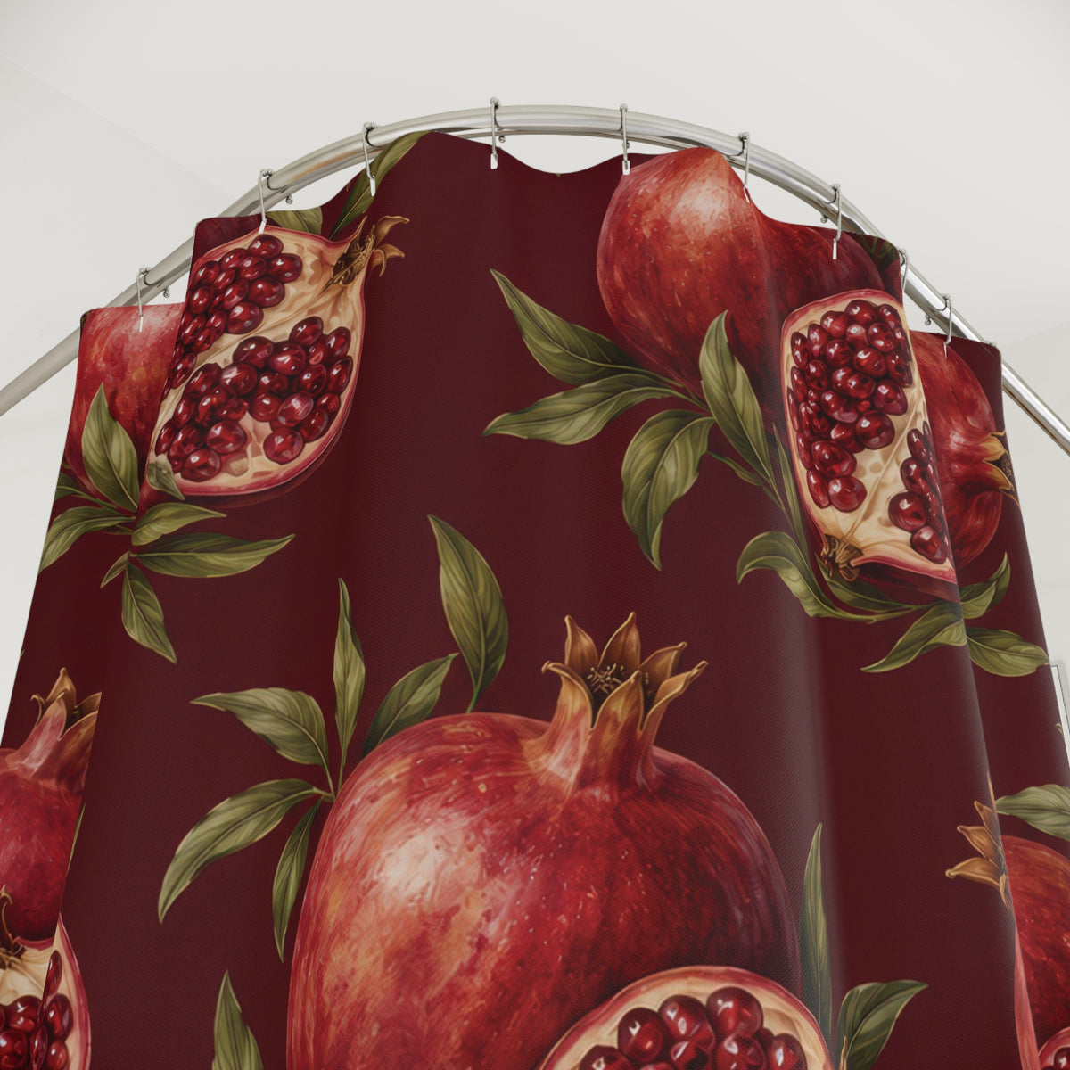 Red pomegranates with ruby seeds and green leaves on maroon shower curtain with close-up print, hooks, and folds