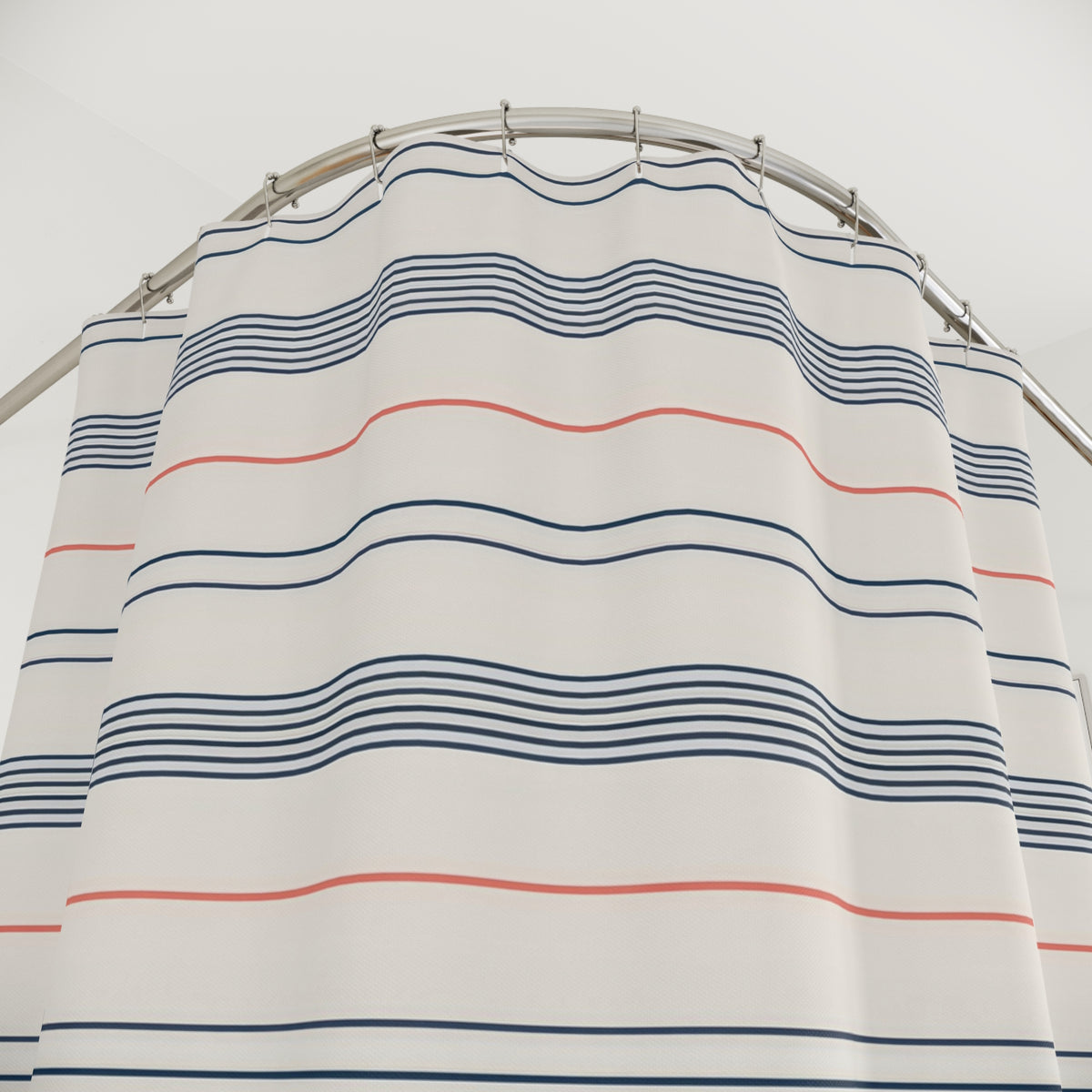 Fine navy line bands and single coral stripes on cream shower curtain with close-up print, hooks, and folds