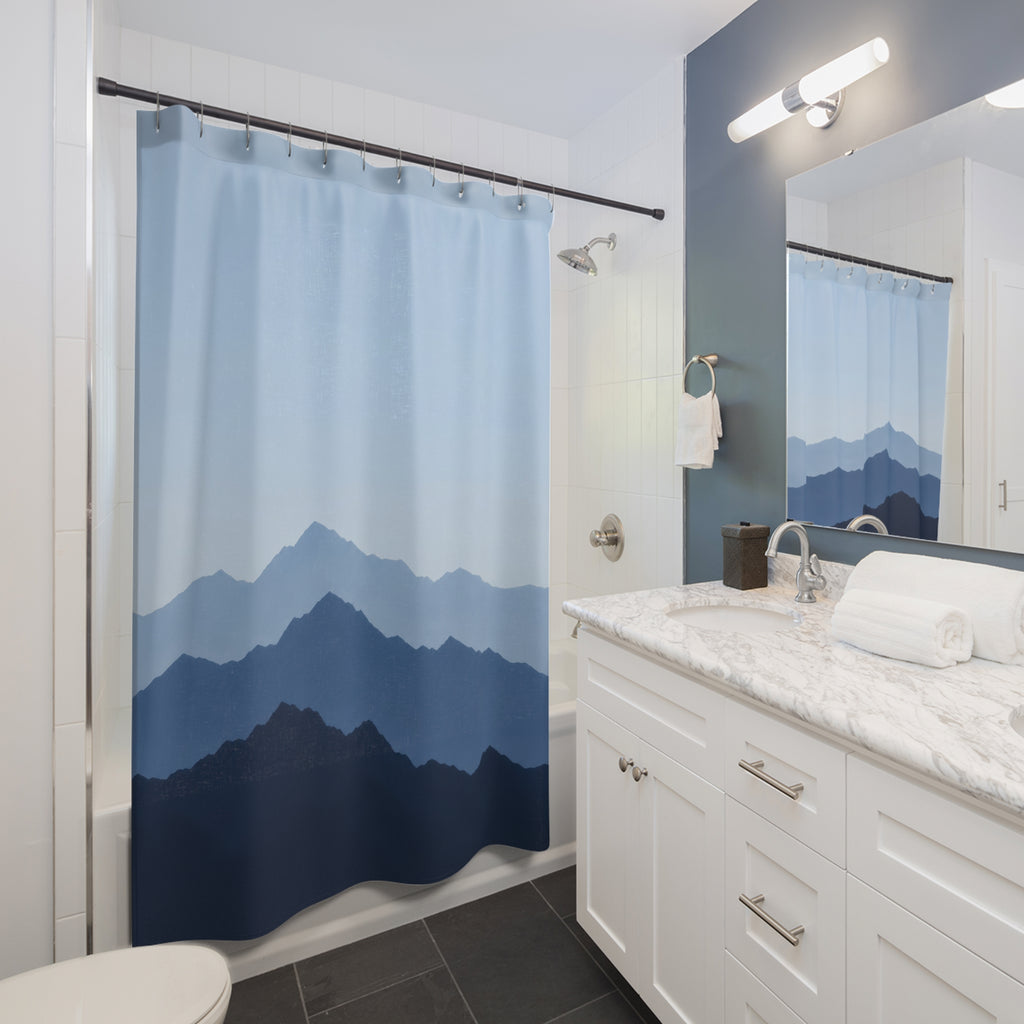 Layered pale blue, slate and indigo mountain ridges shower curtain beside a white vanity