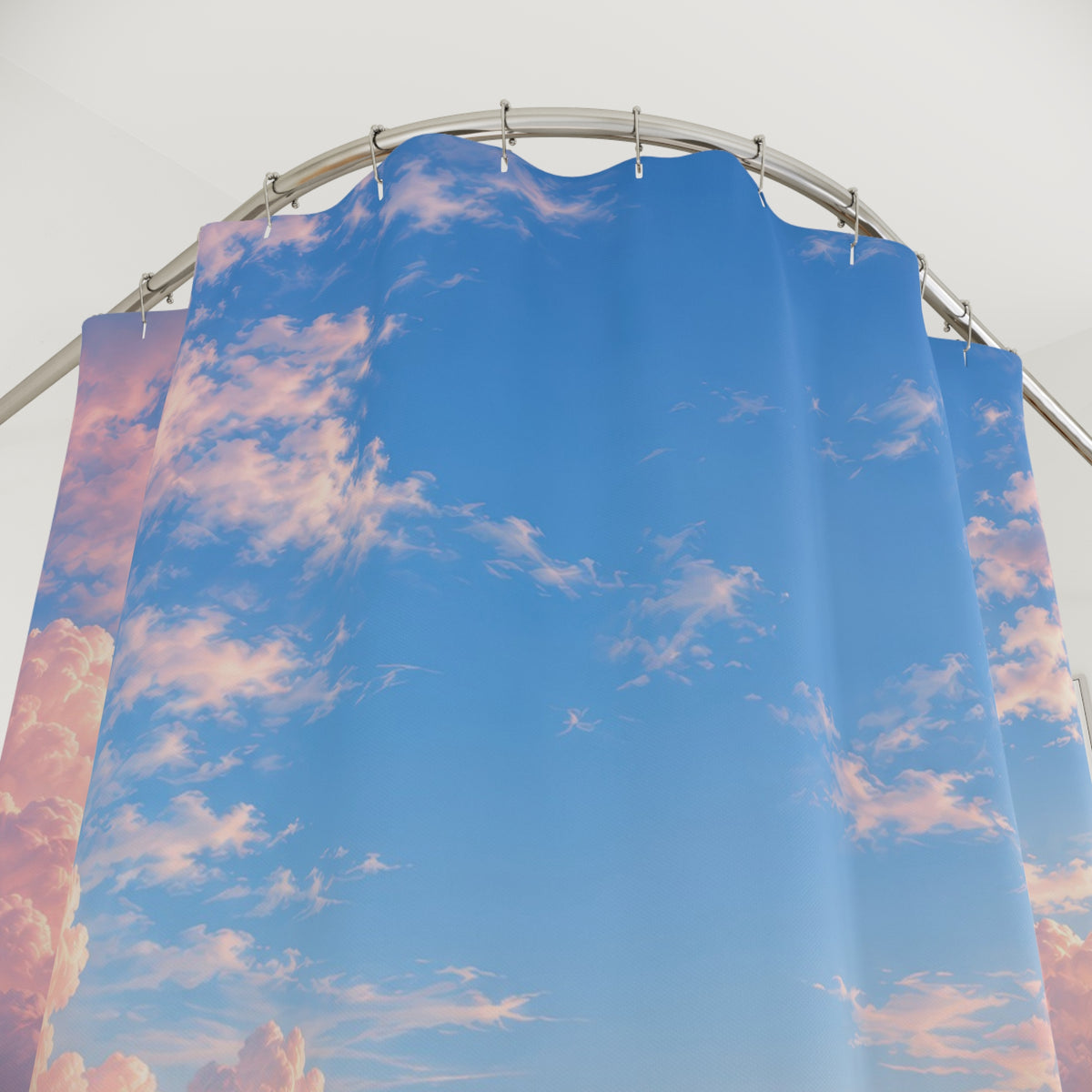 Pink cumulus clouds around an open blue sky shower curtain with close-up print, hooks, and folds