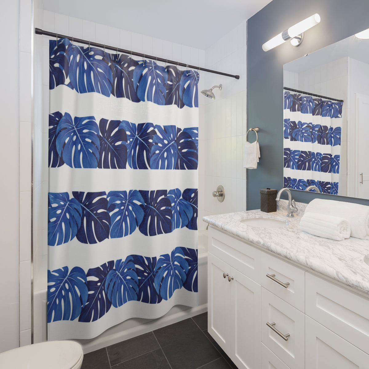 Cobalt monstera leaf bands alternating with white stripes shower curtain beside a white vanity