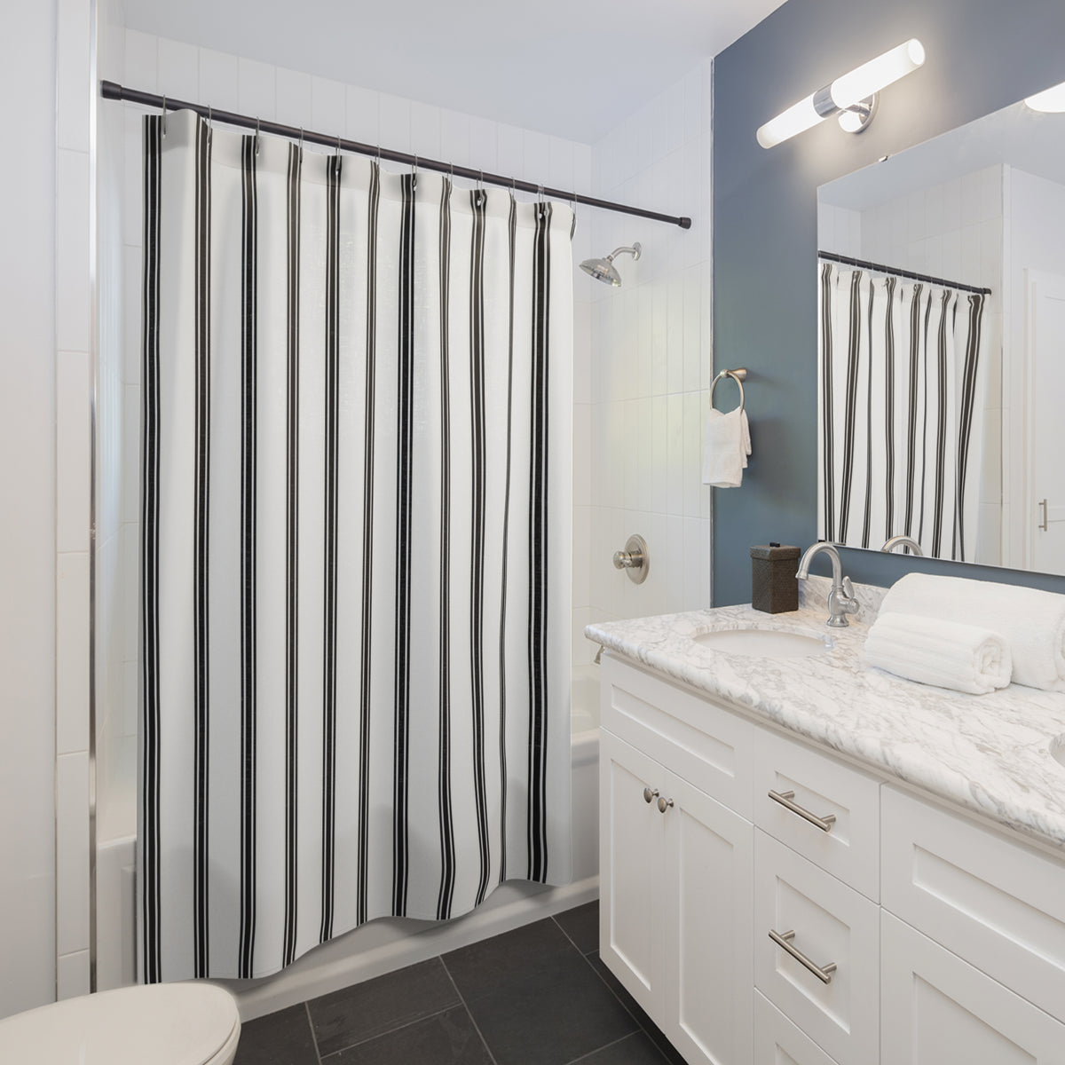 Fine black ticking stripe trios on white shower curtain beside a white vanity